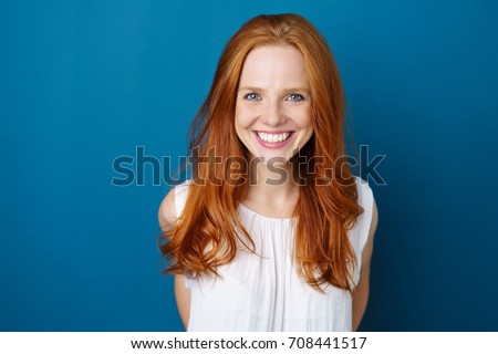 Portrait of young red-haired smiling woman against blue background