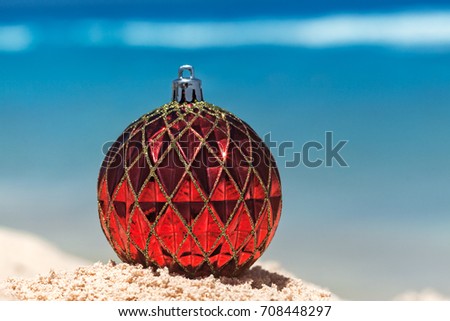 Red Christmas ball on yellow sand at tropical beach and sea as a background, holiday concept