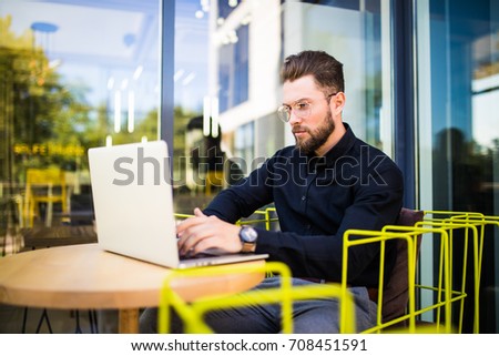 Handsome businessman using modern laptop outdoors, manager working in cafe during break and searching information in internet on his notebook computer