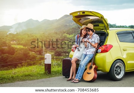 Couple of traveler sitting on hatchback of car and looking at the picture on camera near the road during holiday.Young couple tourist enjoying on vacation. 