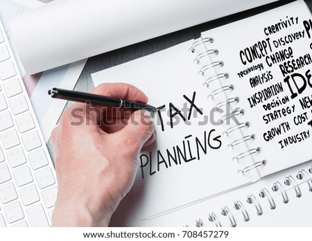 Hand writing in notepad placed on desktop with keyboard and other items. Tax planning concept 