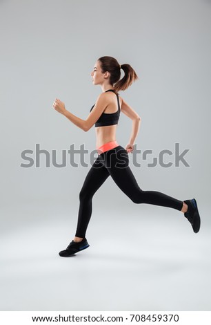 Full length picture of a sports woman running in studio over gray background