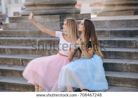 Two beautiful girls in colored skirts sit on stairs