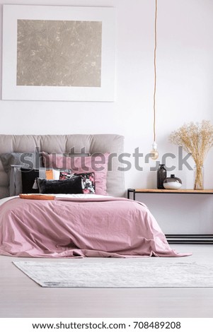 Decorative vases on table in stylish bedroom with copper plate and pink bedsheets on king-size bed