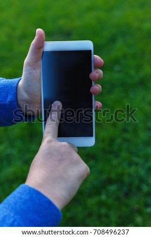 A smartphone in the hands of a teenage girl on a background of green grass/a teenage girl uses her mobile phone in the street