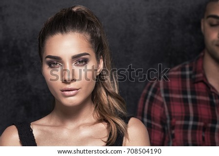 Photo of beautiful caucasian young woman with glamour makeup standing in front of handsome boy in checkered shirts.