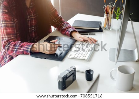 Young asian female designer using graphics tablet while working with computer at studio or office.