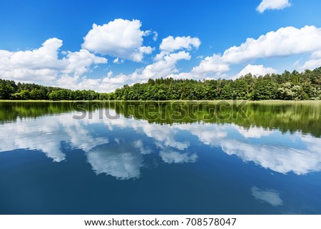 Lake landscape. Summer view of the lakeshore with white clouds reflecting in the water. Royalty-Free Stock Photo #708578047