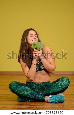 Sportive beautiful girl with broccoli. Yellow background