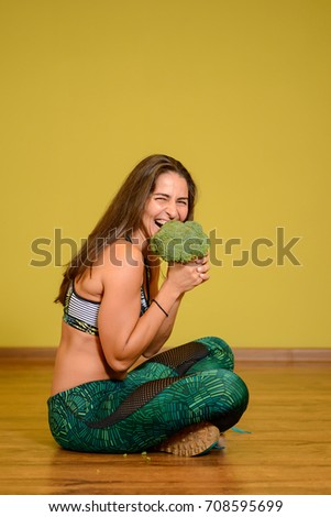Sportive beautiful girl with broccoli. Yellow background
