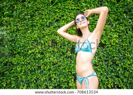 Happy woman in bikini posing against green bush