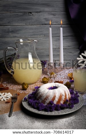 A top view of a beautiful table setting from holidays food on a gray wooden background. Traditional homemade cake with icing and decorative flowers on a plate. Pineapple juice and candles on a table.