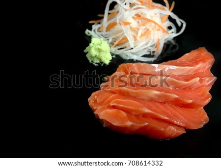 Sashimi salmon with wasabi and shredded radish are on the black ceramic dish background. Selective focus. Isolated picture.
