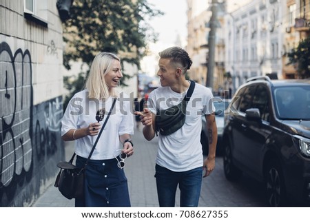 Attractive trendy hipster millennial couple or two friends walk on street in urban city, they laugh and giggle, make jokes and enjoy youth and life