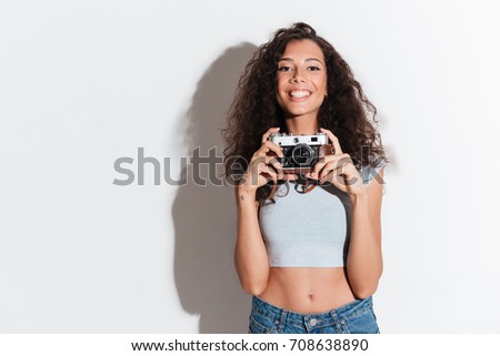 Cheerful young woman with photocamera looking and smiling isolated over white
