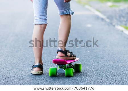 Young girl riding on skateboard on the road. Detail shot of legs, selective focus, smooth background.