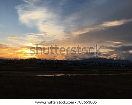 landscape scenery colorful golden sunset behind the hill. the sky a bright blue behind the white clouds. the foreground building and the land free 