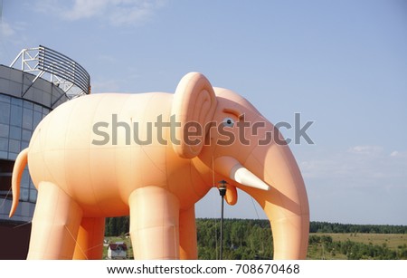 Inflatable pink elephant with white tusks against the blue sky tied ropes