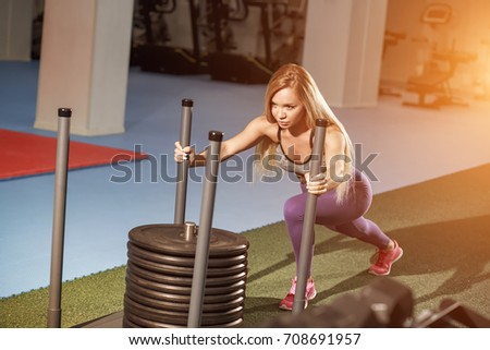 Muscular and strong young female pushing the prowler exercise equipment on artificial grass turf. Fit woman exercising