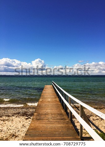 Wooden pier in the south of Sweden on a sunny day. Denmark on the other side beneath the clouds.