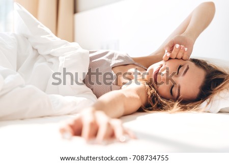 Image of young smiling pretty lady lies in bed indoors. Eyes closed. Royalty-Free Stock Photo #708734755