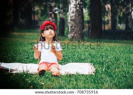 Portrait of little girl blowing soap bubbles and looking on one of them