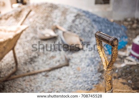 A handle of a shovel with a barrow, hoe, hod, and rocks in the background