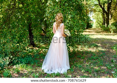 Beautiful bride in long wedding dress with bridal bouquet of flowers walking in the park outdoor. Happy bride in wedding dress on summer day, free space