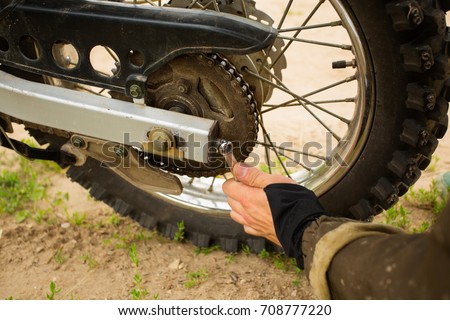Man adjusting bolt with socket wrench on rear motorcycle wheel. Bike rider fixing his ride by tightening metal parts. Close up detailed view at parts of dirt bike vehicle, daytime setting.