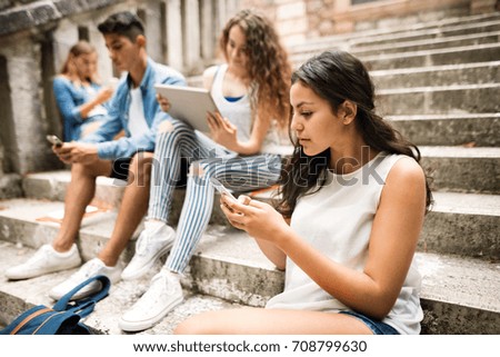 Teenagers with smartphones and tablets on stone steps.