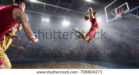 Basketball players on big professional arena during the game. Basketball player makes slam dunk. Players are wearing unbrand clothes.