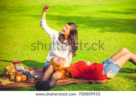 Two girls take a selfie in the park. Friendly picnic on a warm autumn day. Girls in knitted sweaters in the nature have fun and rest