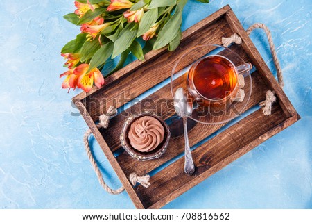 Image of wooden tray with cup of tea, cake with orange flowers on blue table
