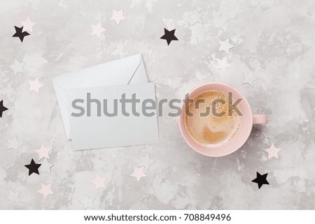 Envelope with empty card and cup of coffee on womans working desk top view. Flat lay. Party invitation or greeting message.
