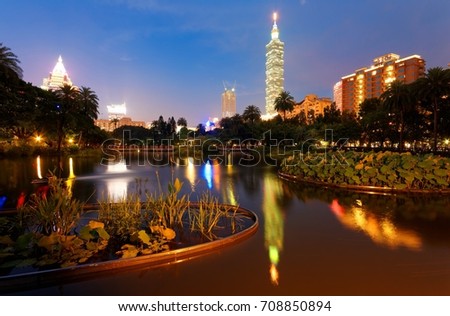 Night scenery of an urban park in Taipei City with the famous landmark 101 Tower reflected on the pond & aquatic plants floating the peaceful water under blue twilight in Downtown Taipei, Taiwan Asia
