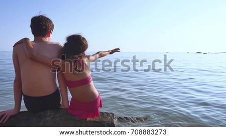 Boy and girl on the sea. A boy and girl are sitting on the rocks on the sea view from the back of a romance happy childhood and dreams