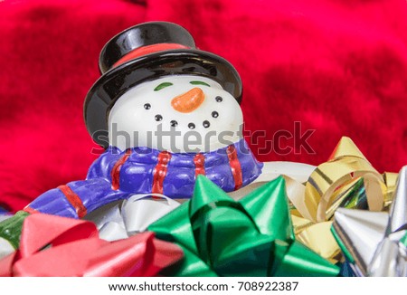 A horizontal closeup photo of a smiling snowman bowl with multicolored bows in it and a red velvet background