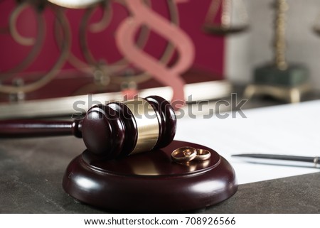 Image of wedding rings on wooden gavel at table in courtroom