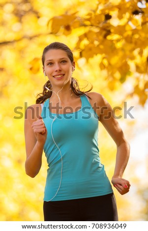 Young brunette woman running in autumn forest, listening to music. Lifestyle and sport photo of healthy style. Outdoor and nature fitness exercise.