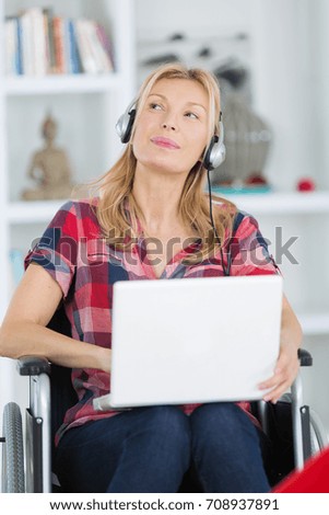 woman in wheelchair using laptop while listening to music