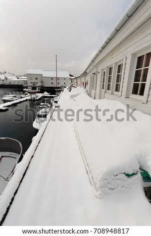 Fishing boats moored at wooden pier on the west side of the fishing port-white warehouses and rorbuer huts-heavy snowfall covering the whole harbor. Hamnoy-Reine-Moskenes-Lofoten-Nordland fylke-Norway