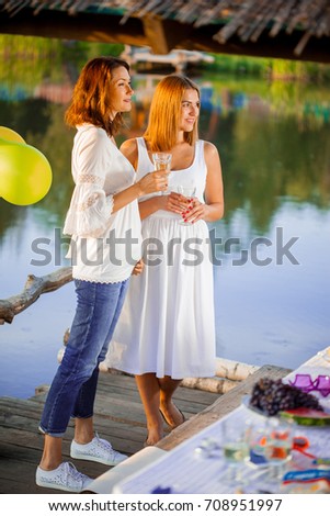 two young beautiful women at a party near the water with glasses of wine