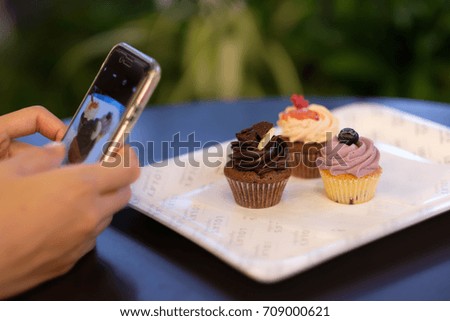 Japanese woman taking pictures of delicious cup cakes with a smart phone.