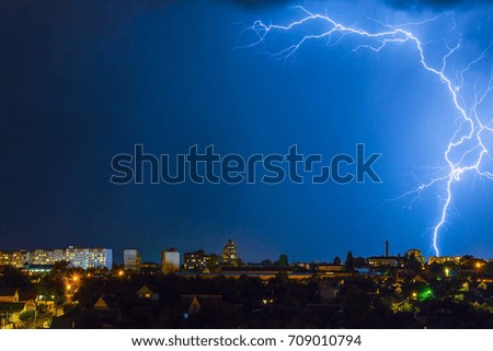 Lightning over the city in the night sky strikes the roof of the house.