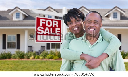 Happy African American Couple In Front of Beautiful House and For Sale Real Estate Sign.