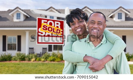 Happy African American Couple In Front of Beautiful House and Sold For Sale Real Estate Sign.