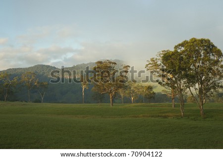 Rural landscape, sun rises with morning mist crossing in distance, Kangaroo Valley, Australia.