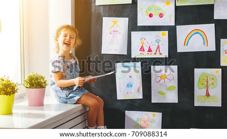 child girl hanging her drawings on the wall
