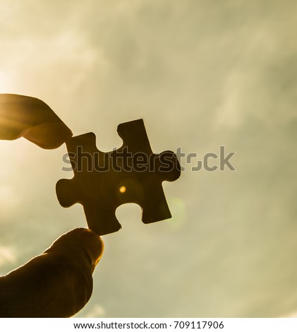 one hand trying to connect puzzle piece with sunset background. Jigsaw alone wooden puzzle against sun rays. one part of the whole. symbol of association and connection. business strategy. copy space