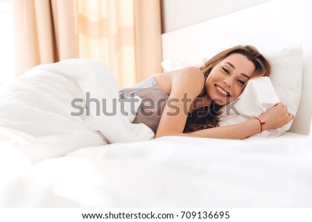 Image of young happy pretty lady lies in bed indoors. Looking camera.